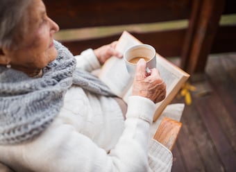 an-elderly-woman-reading-book-outdoors-on-a-terrac-2021-08-26-12-09-08-utc